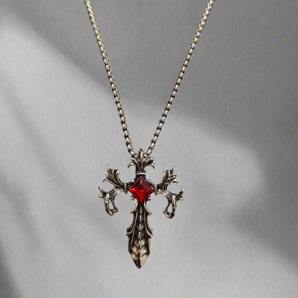 A stainless steel pendant with a deep red synthetic ruby, designed in a gothic style, attached to a box chain.